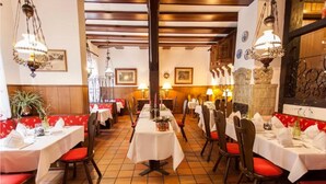 A restaurant with multiple tables and booths, each with white tablecloths and red cushioned chairs. - Hotel Alter Wolf (Wolfsburg)