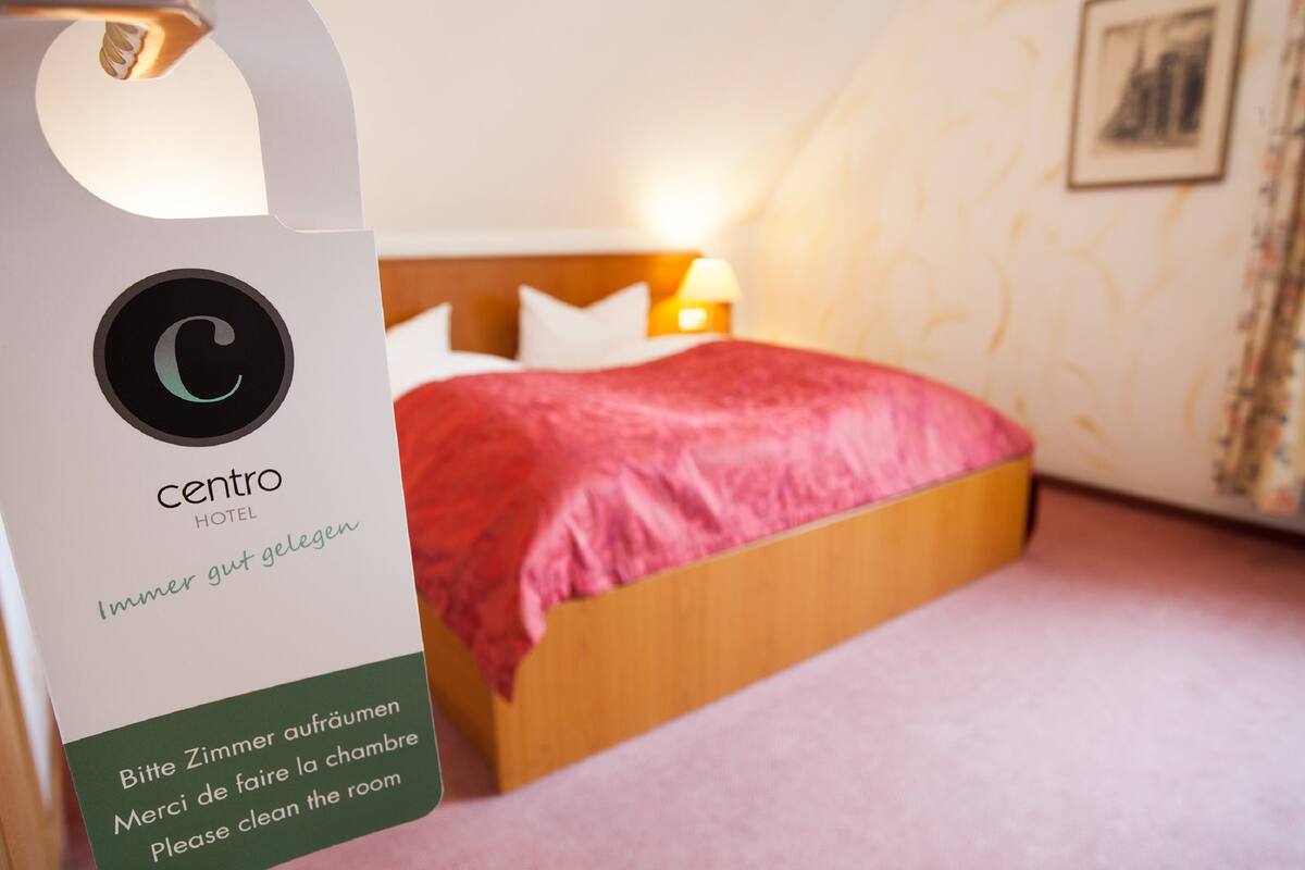 A hotel room with a bed, a nightstand, and a wall-mounted lamp.