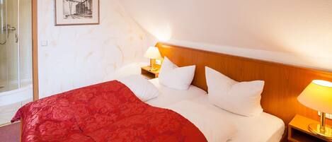 Habitación de hotel con una cama grande, cabecera de madera, mesita de noche con lámpara y un cuadro en la pared.