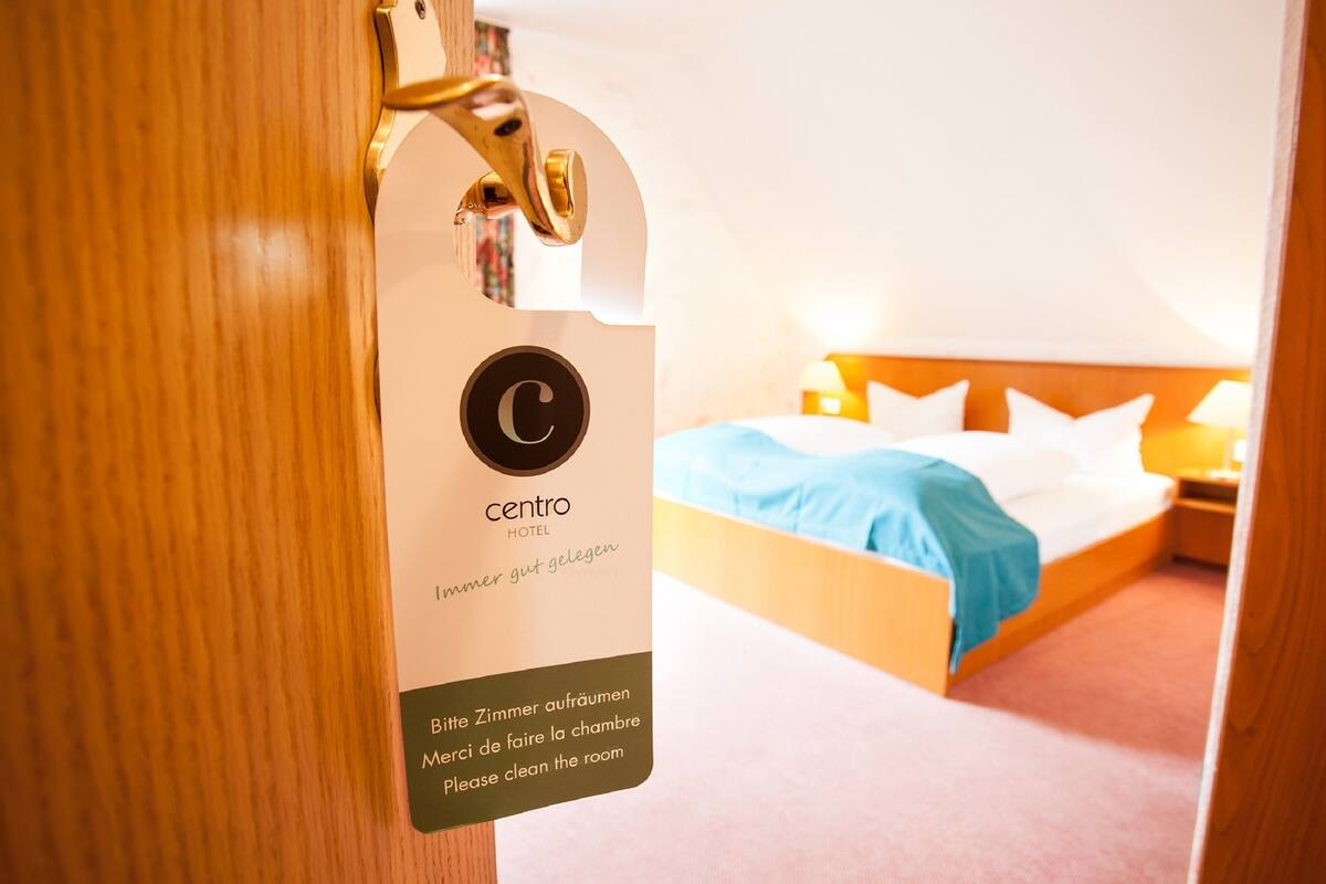 A hotel room with a bed, a nightstand, and a sign indicating the room number and a request to clean the room.