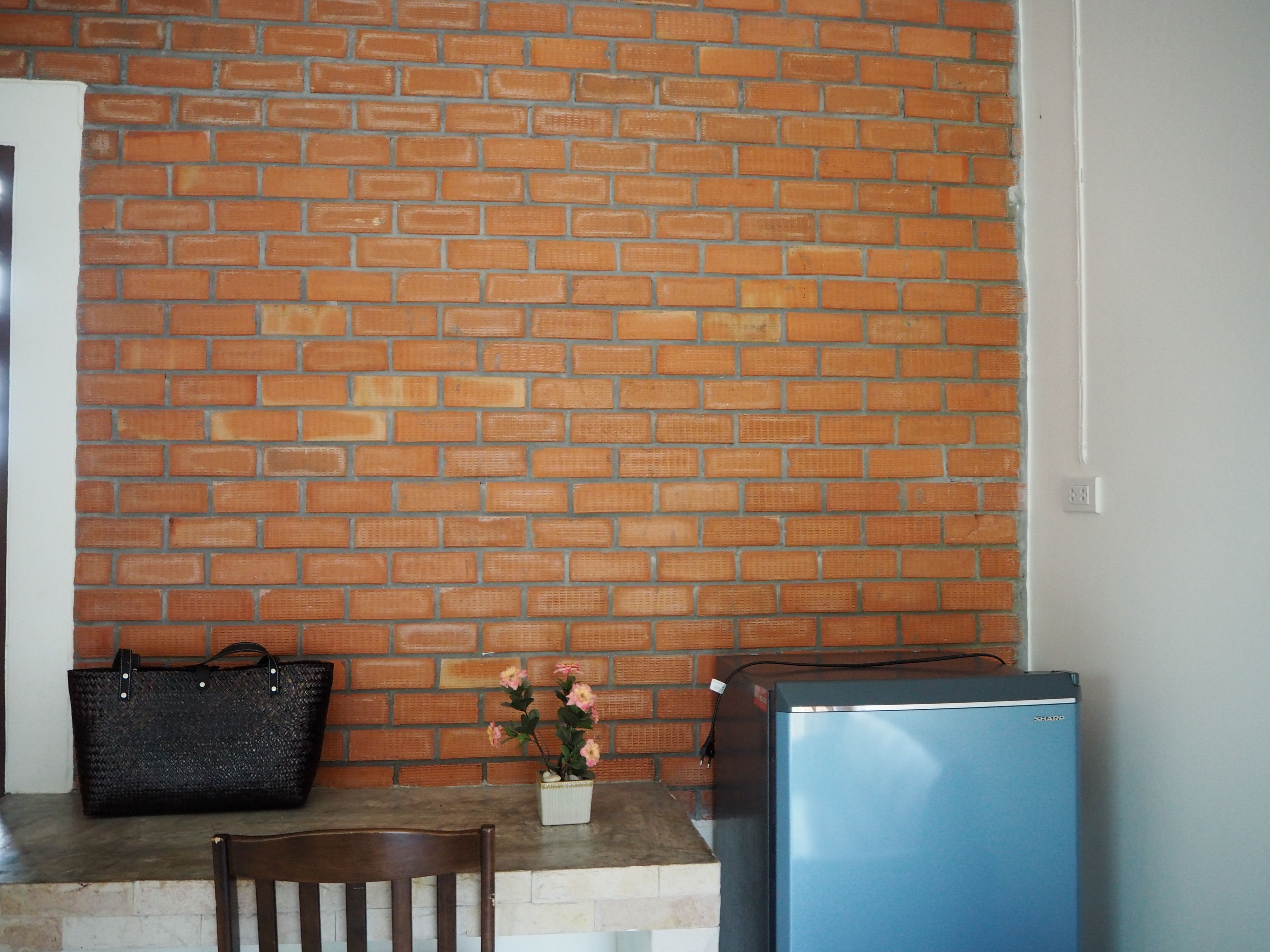 A kitchen with a brick wall, a wooden chair, a black handbag, a small potted plant, and a blue refrigerator.
