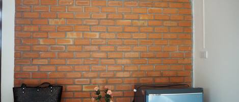 A kitchen with a brick wall, a wooden chair, a black handbag, a small potted plant, and a blue refrigerator.