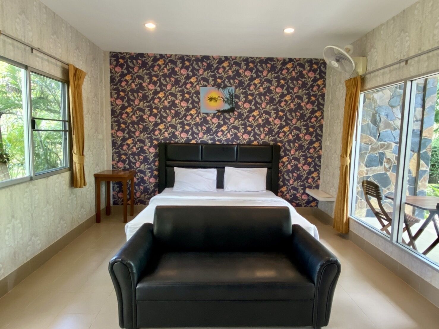 A bedroom with a large bed, a black leather chair, a small table, and a window with curtains.