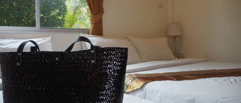 A hotel room with a bed, a window with curtains, and a black woven bag on the bed.
