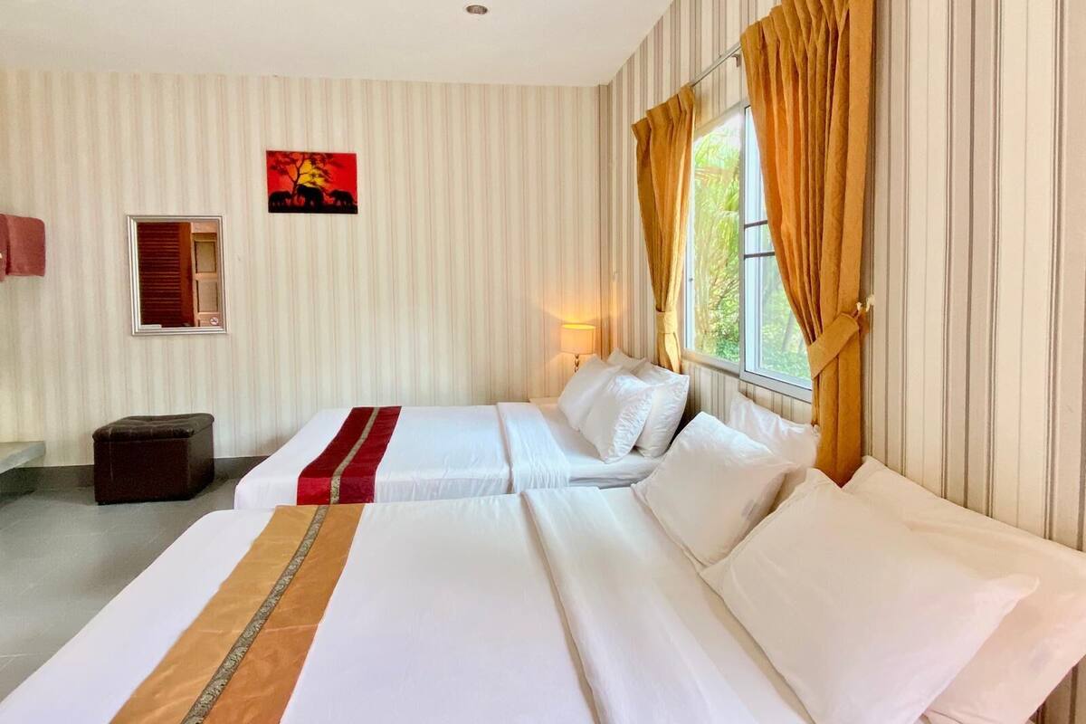 A hotel room with two beds, striped wallpaper, a window with curtains, a nightstand, a lamp, and a painting on the wall.