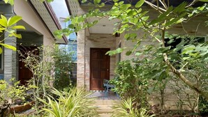 A house with a stone facade, a wooden door, and a garden with various plants and a metal bench. - Canal Resort (Sa Khu)
