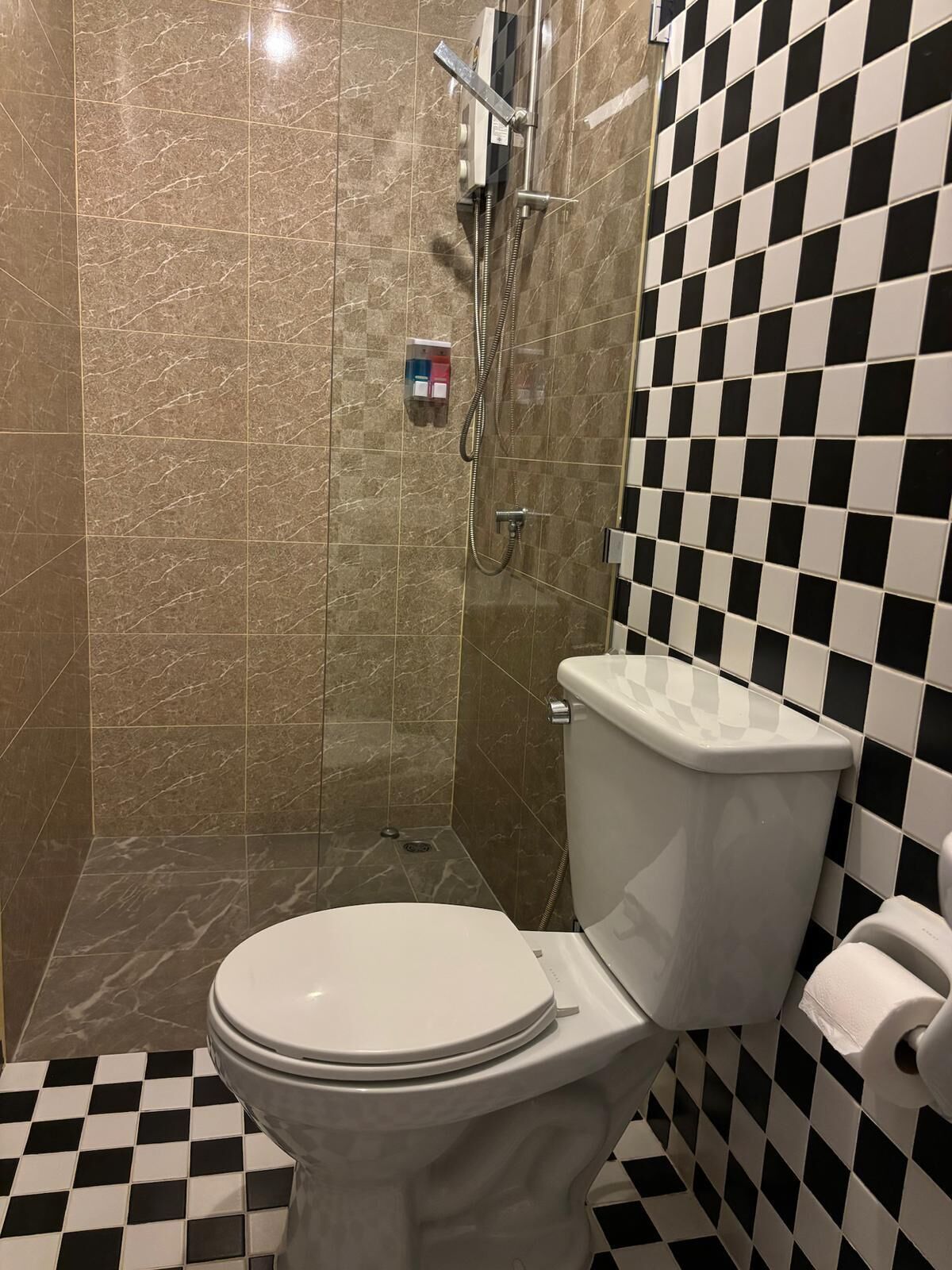 Un baño con piso a cuadros, inodoro, ducha con panel de control y pared de azulejos.