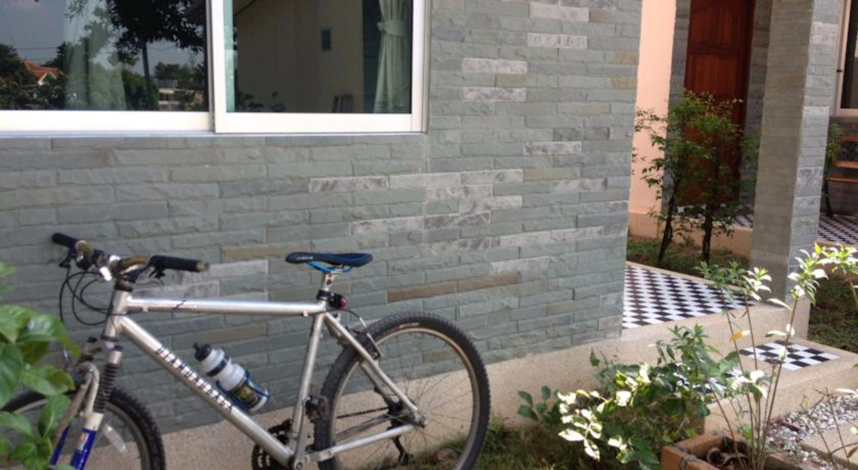 Una bicicleta estacionada frente a un edificio con fachada de piedra, una ventana y un patrón de baldosas a cuadros cerca de la entrada.