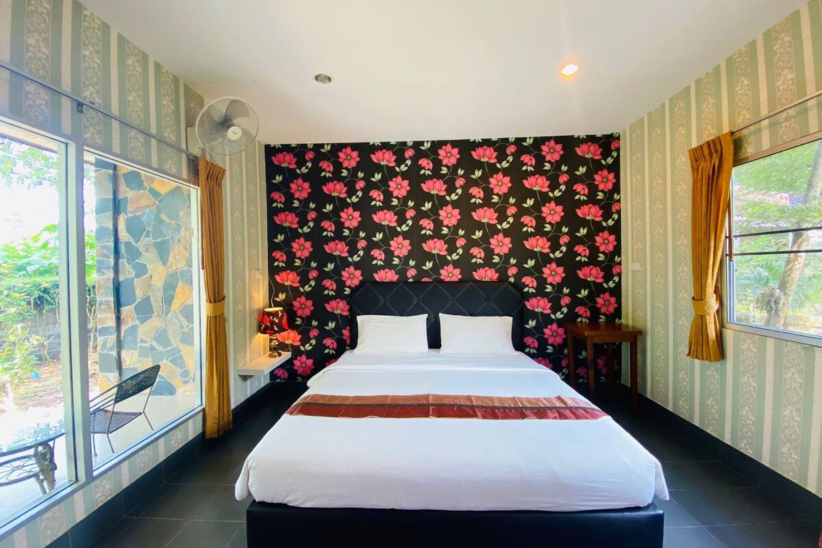 A bedroom with a bed, a window, a fan, and a nightstand.