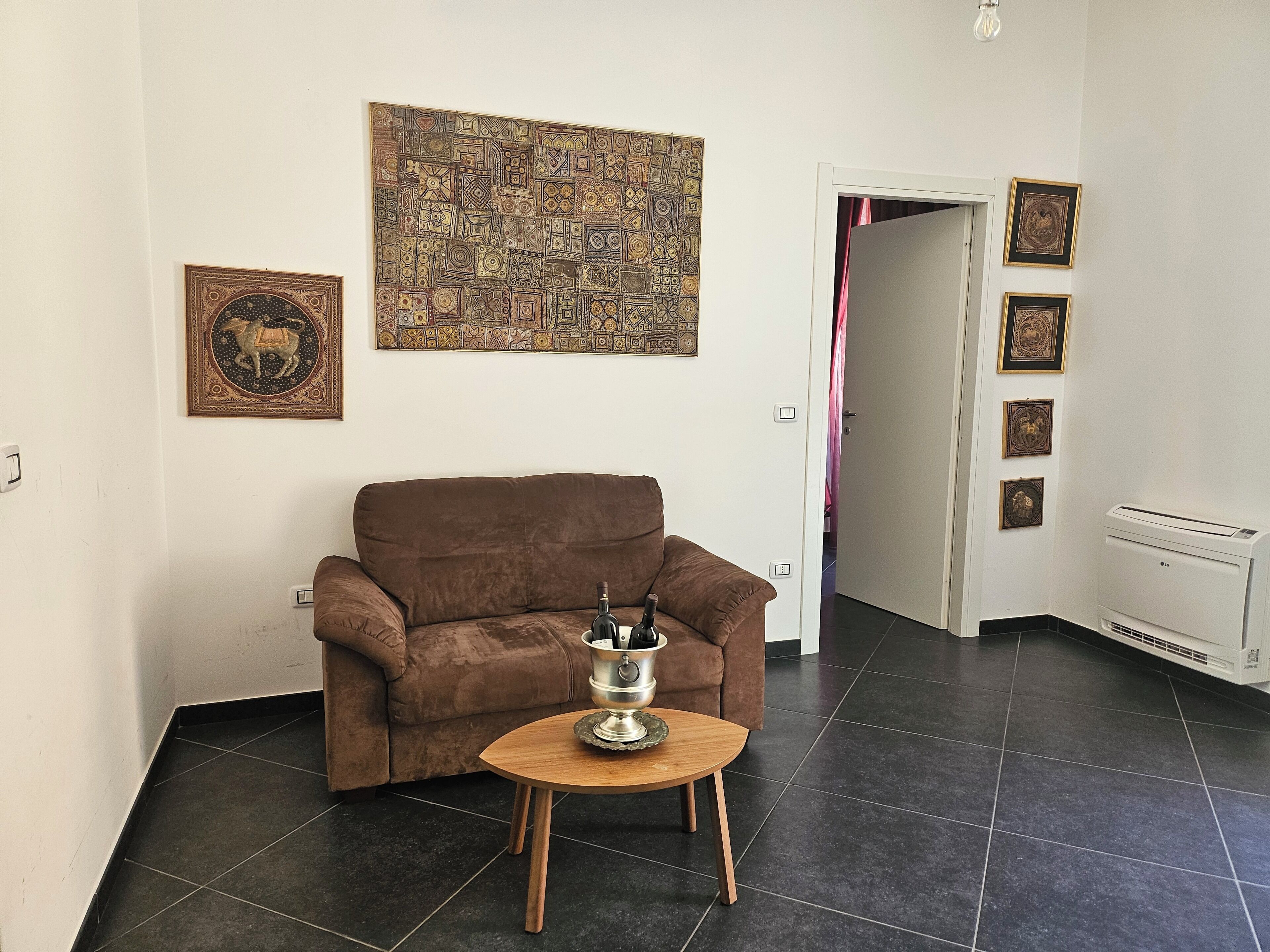 Un soggiorno con un divano marrone, un tavolino di legno con un contenitore argentato, un'opera d'arte decorata e un termosifone.