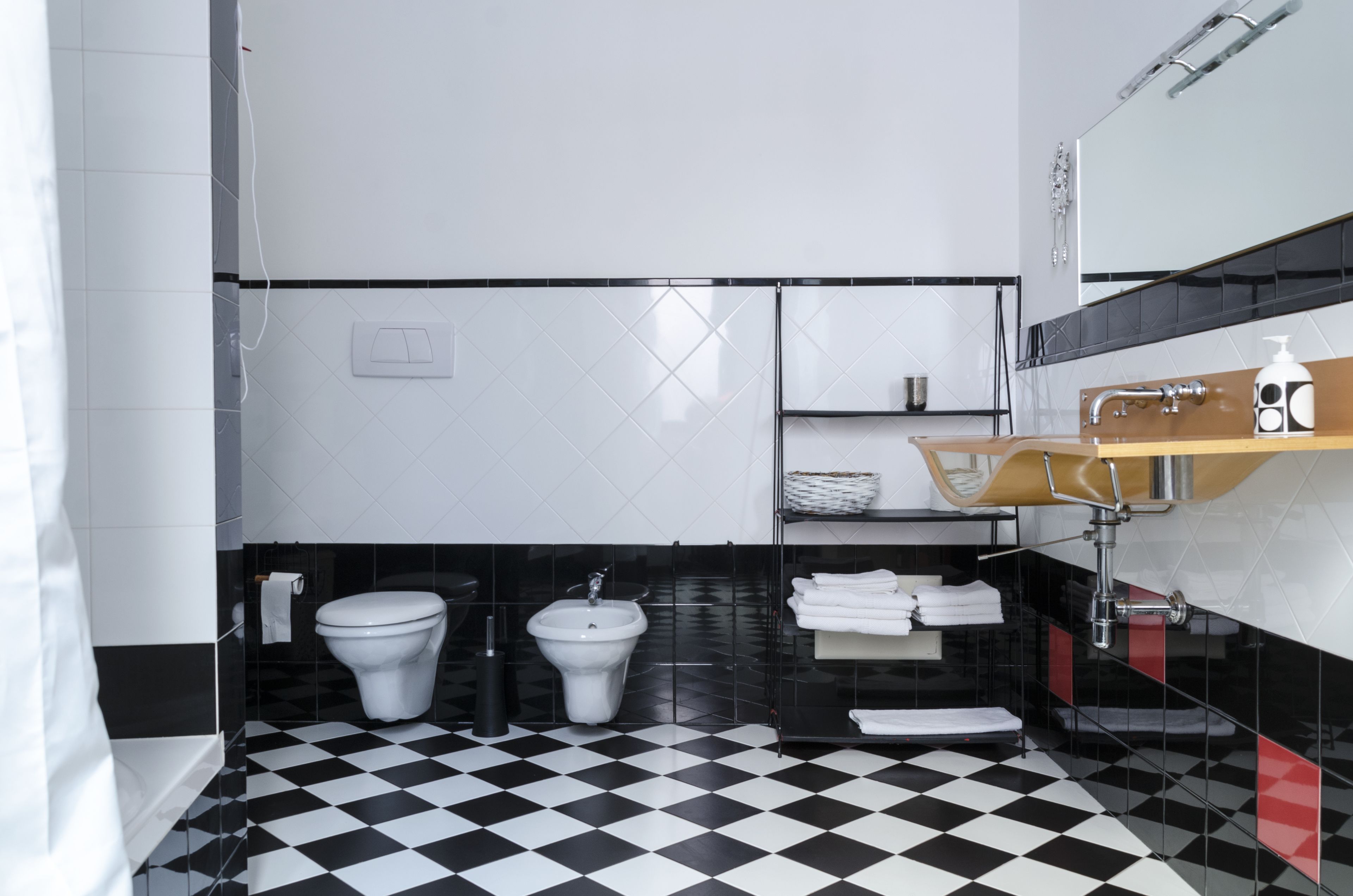 Ein modernes Badezimmer mit einem schwarz-weiß karierten Boden, Toilette, Bidet und einem Waschtisch mit Spiegel und Ablagen.