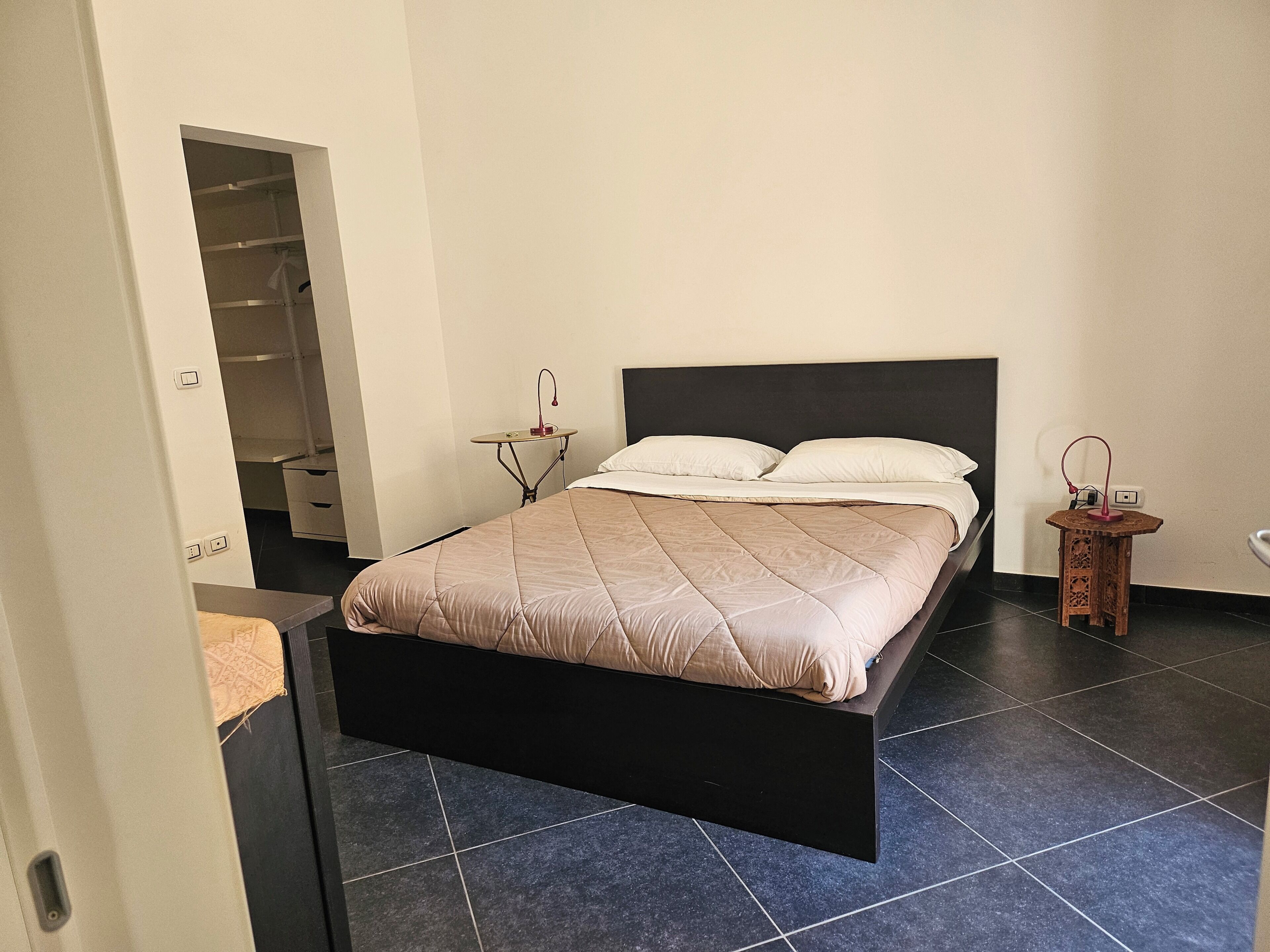 Un dormitorio con cama, mesitas de noche, un armario y una pequeña mesa con lámpara.