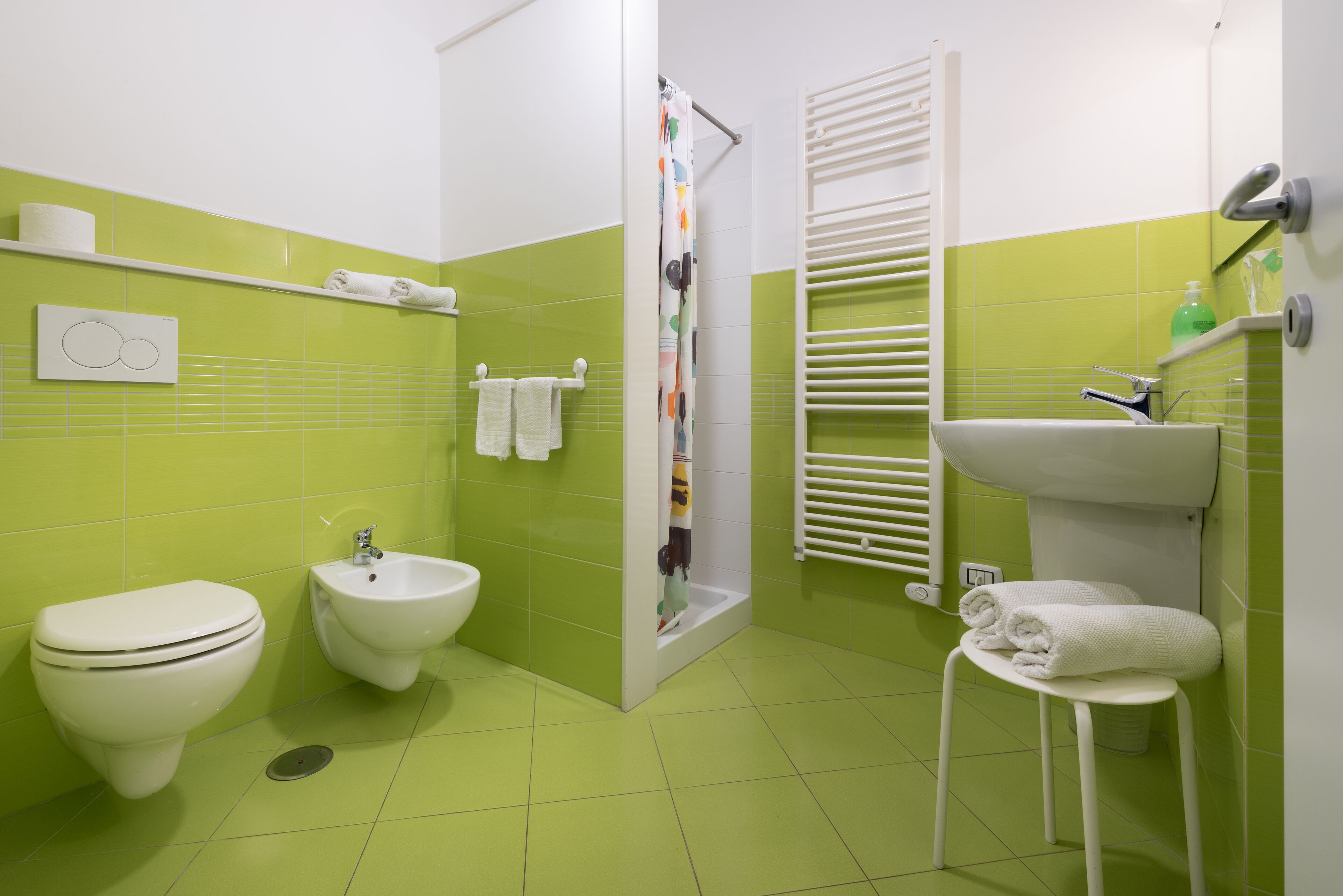 Un baño con inodoro, bidé y lavamanos, con azulejos verdes y sanitarios blancos.