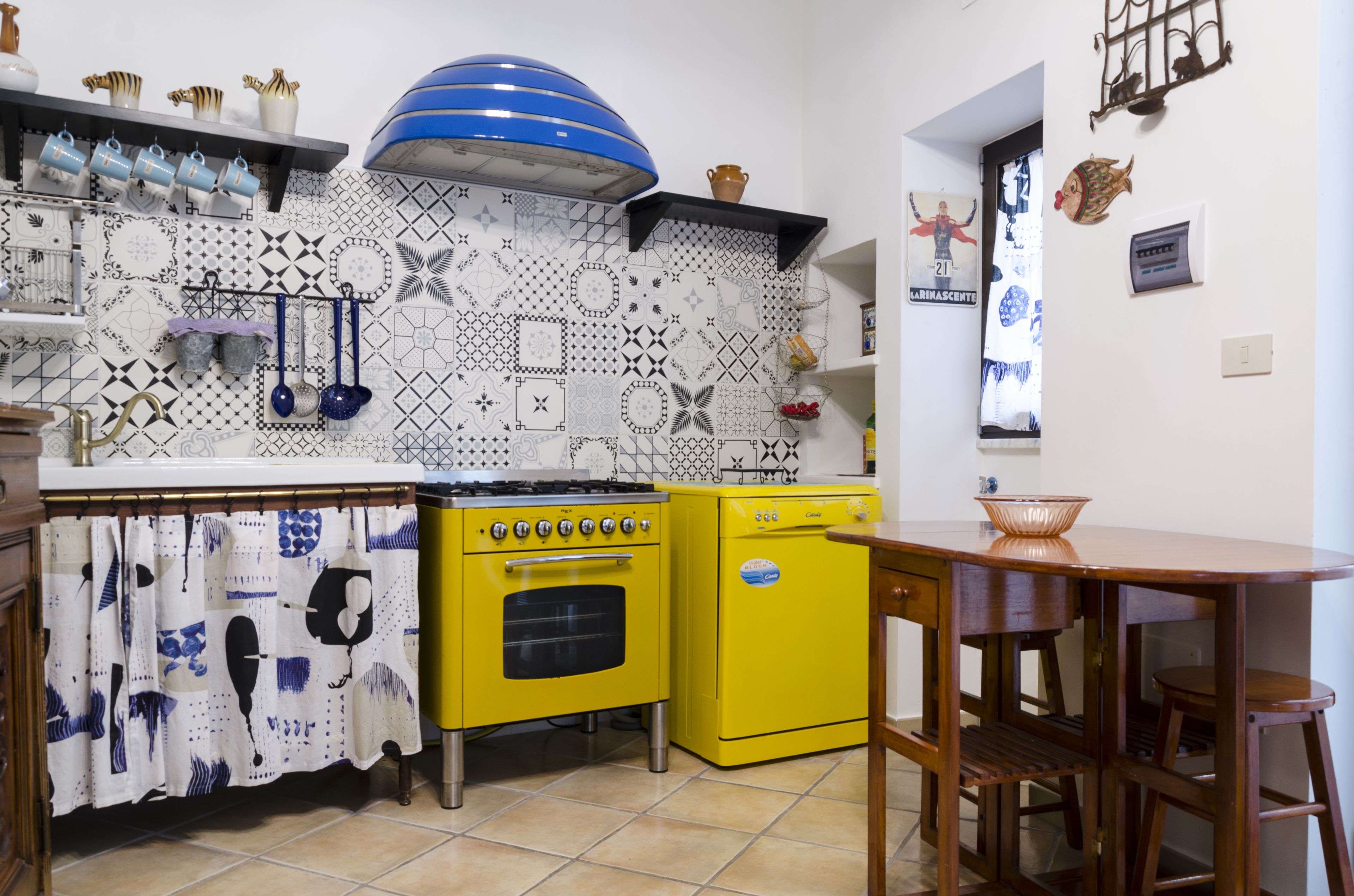 Een keuken met een gele kookplaat, een blauwe afzuigkap en een achterwand met een patroon.
