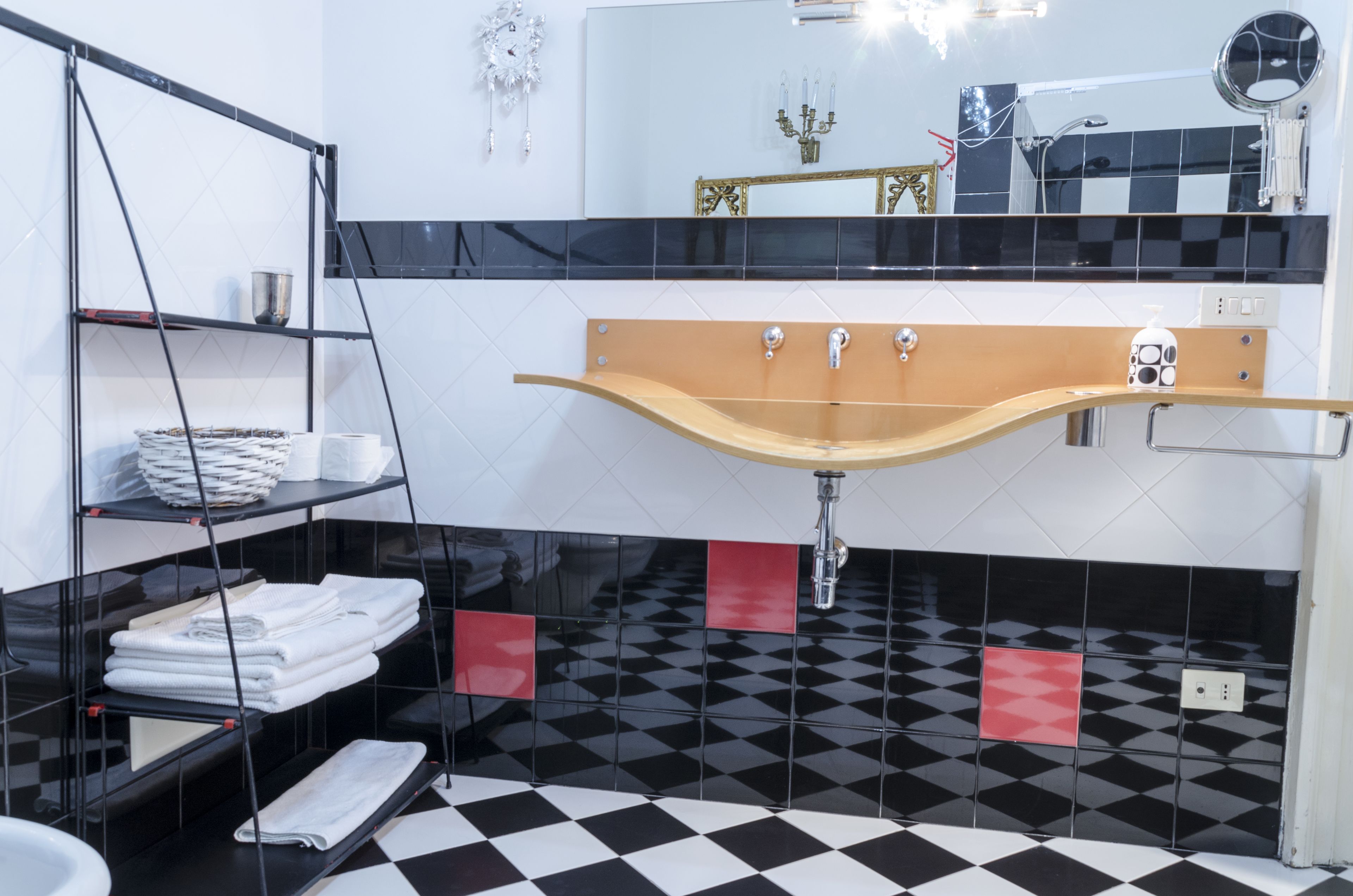 A bathroom with a black and white checkered floor, a wooden vanity with a mirror, and shelves with towels.