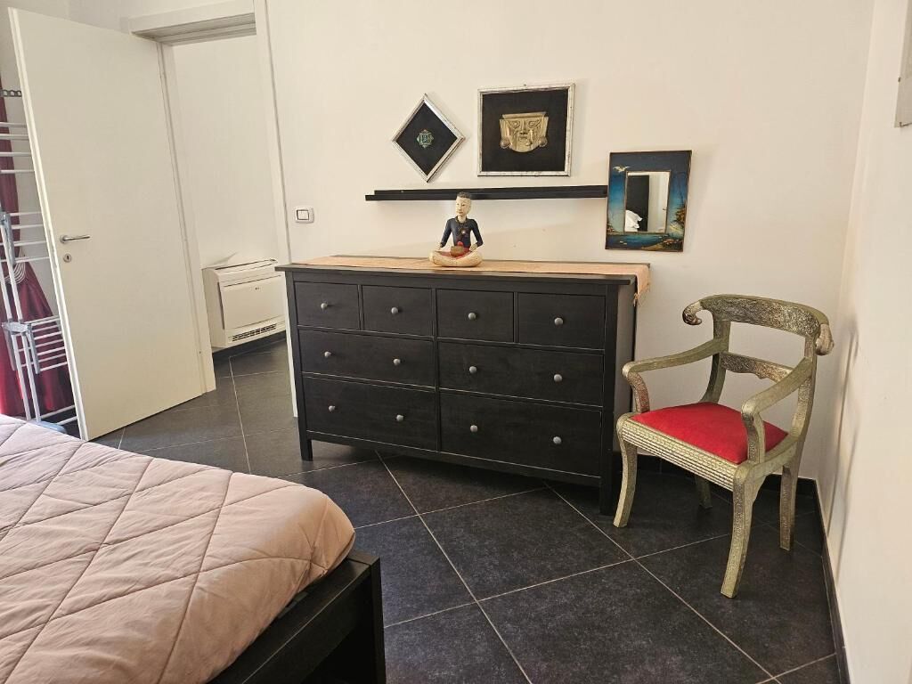 A bedroom with a bed, a dresser, a chair, and wall-mounted artwork.