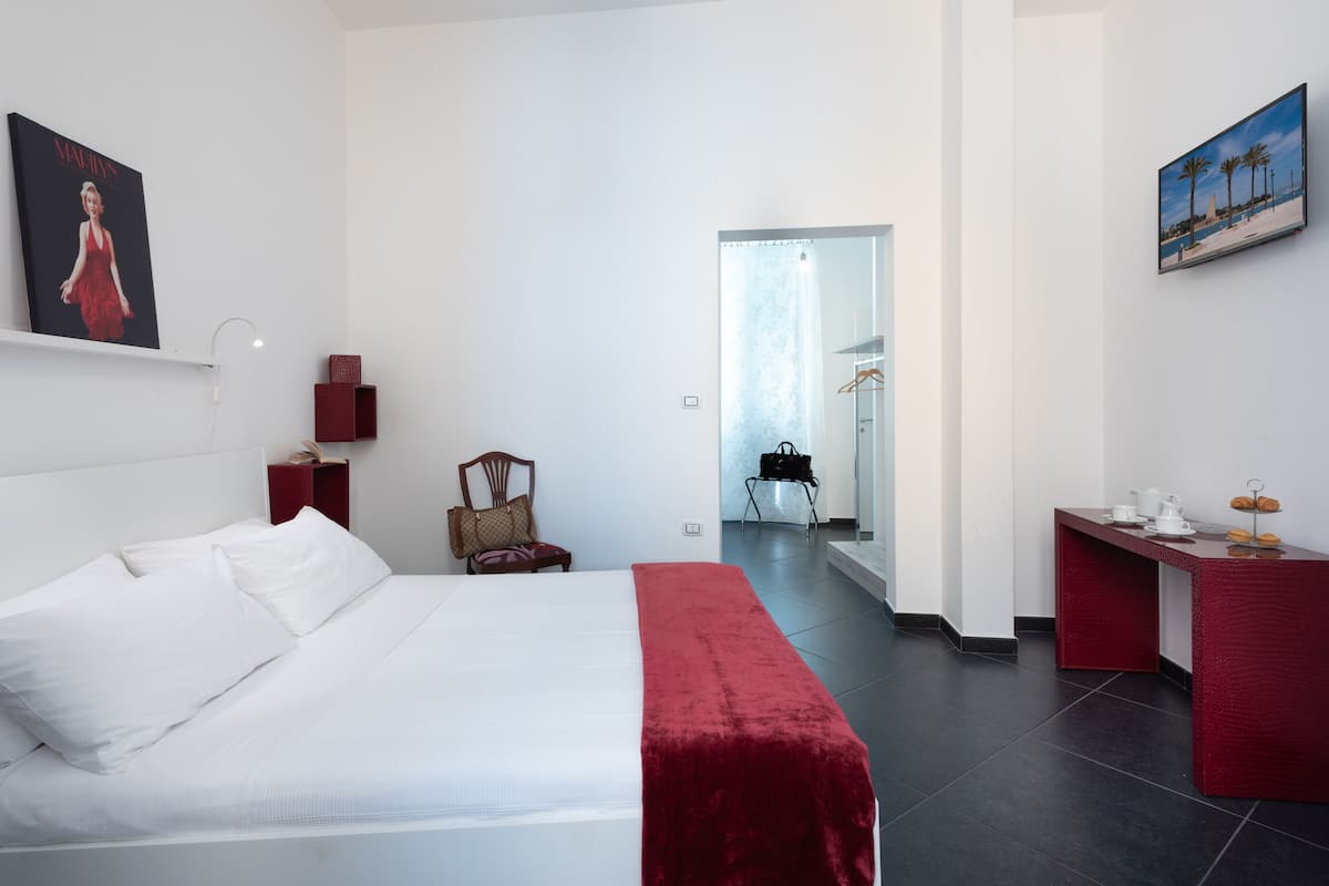 Een hotelkamer met een groot bed, een rode bank, een bureau met een stoel en een schilderij aan de wand.