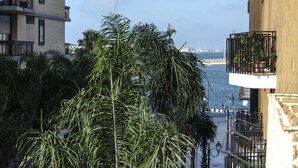 A coastal building with balconies overlooking the sea, surrounded by palm trees.