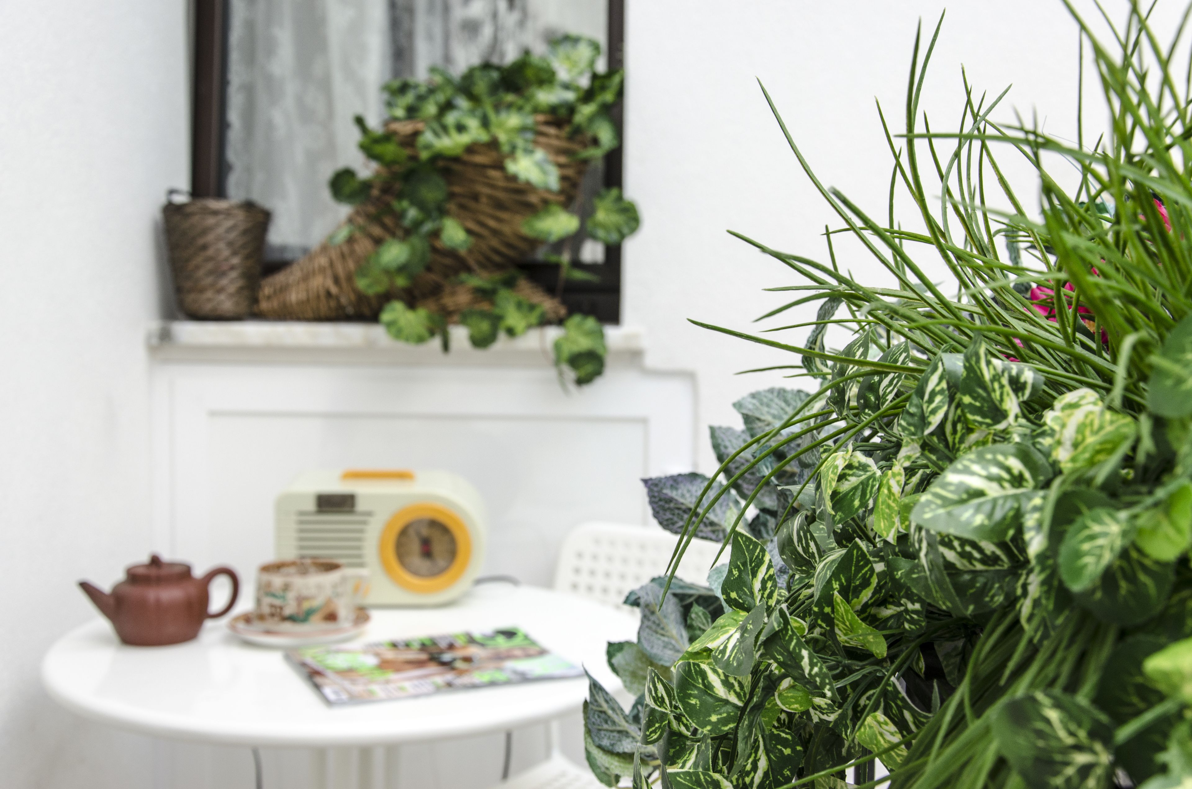 Una habitación acogedora con una mesa blanca, una tetera marrón, una radio amarilla y una ventana con plantas verdes.