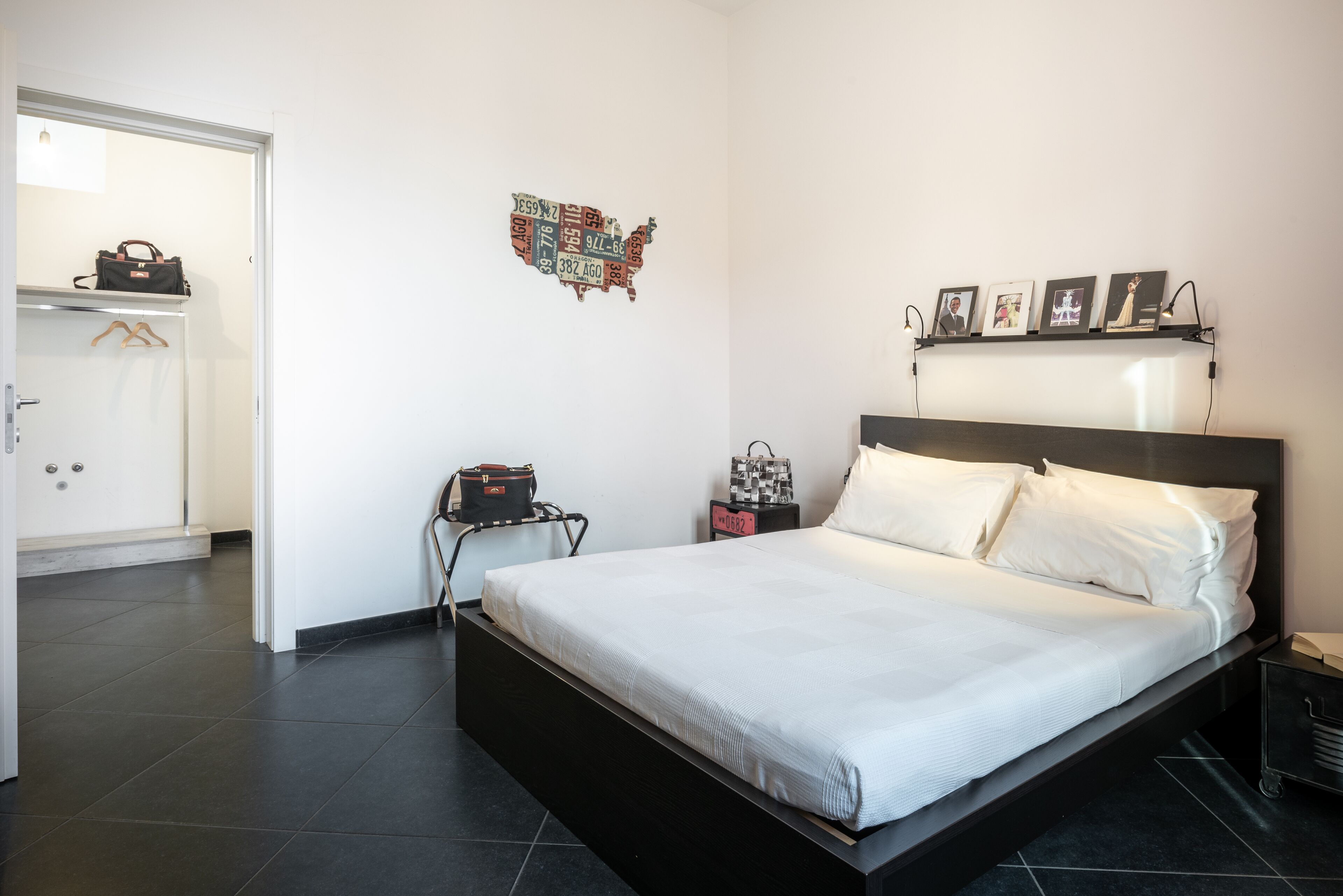 Ein modernes Schlafzimmer mit einem großen Bett, einer Wandkunst mit einer Karte, einem Nachttisch mit einer Uhr und einem Kleiderschrank mit einer aufhängbaren Tasche.