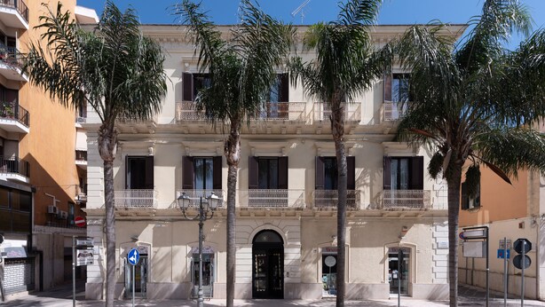 A multi-story building with balconies, palm trees, and a clear blue sky.