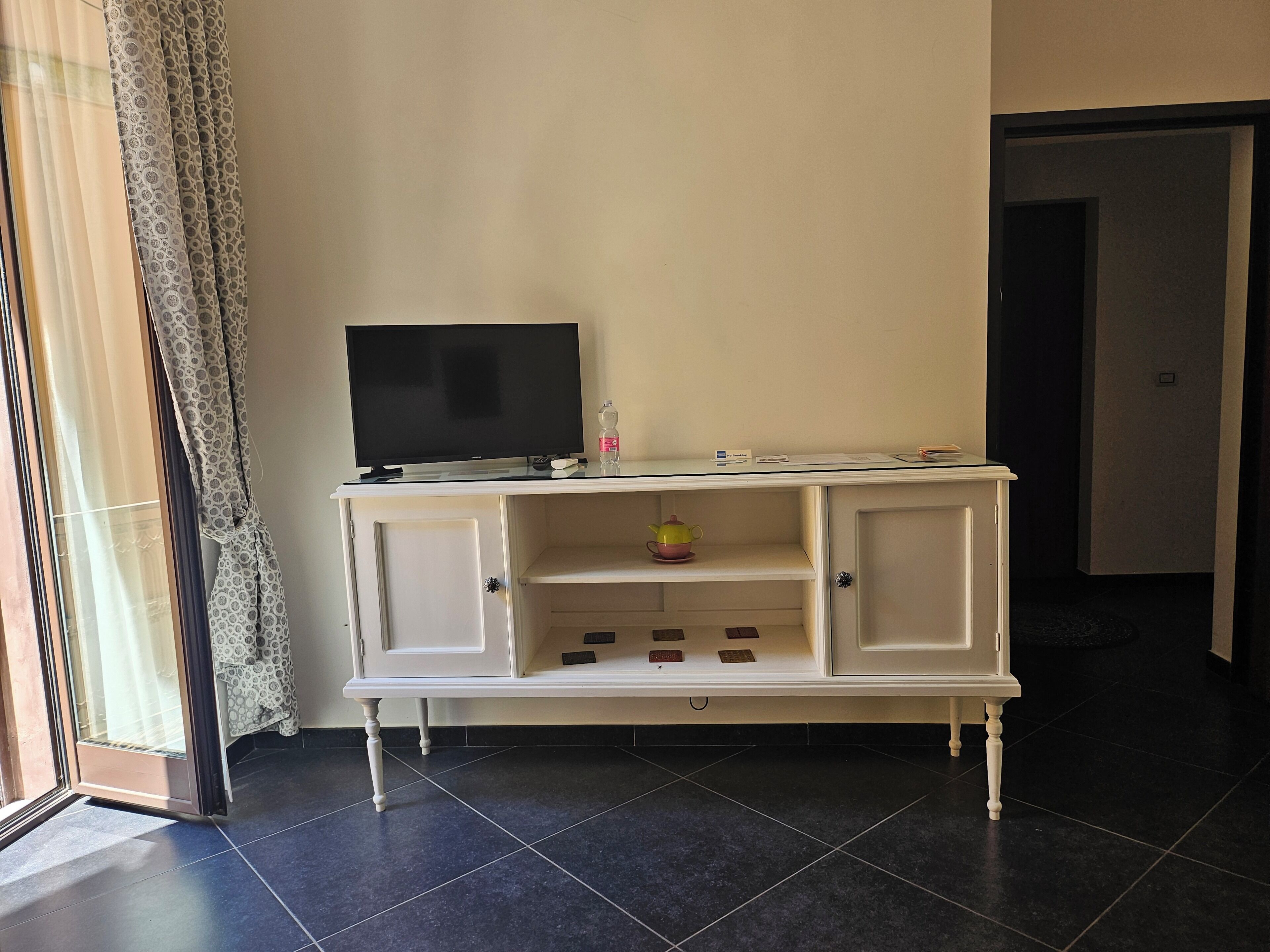 A white TV stand with a flat-screen TV, a small shelf with a teapot, and a door leading to another room.