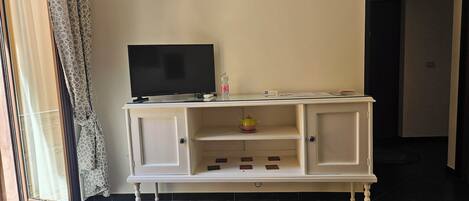 A white TV stand with a flat-screen TV, a small shelf with a teapot, and a door leading to another room.
