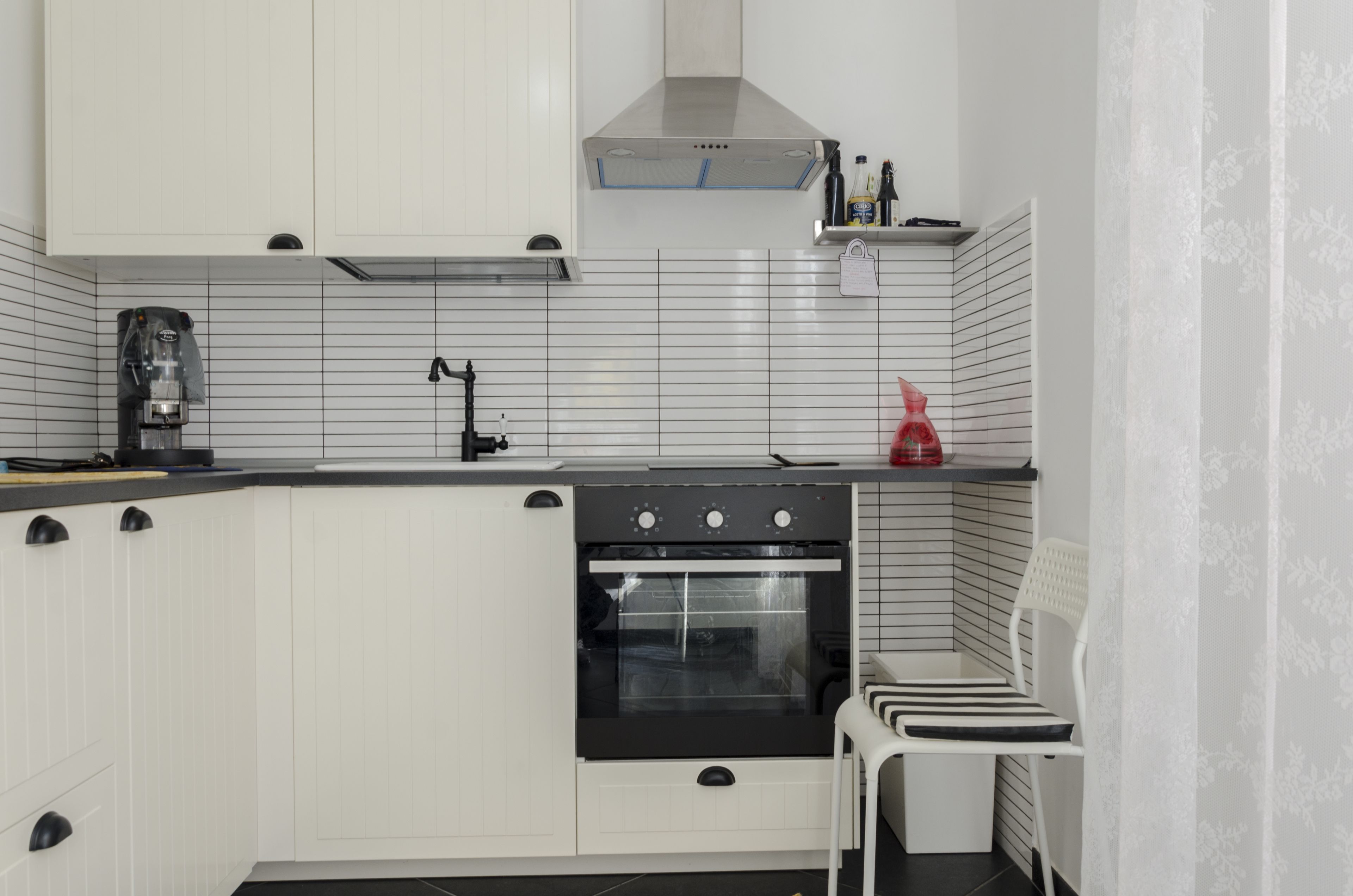 A modern kitchen with white cabinets, a black stove, and a coffee machine.