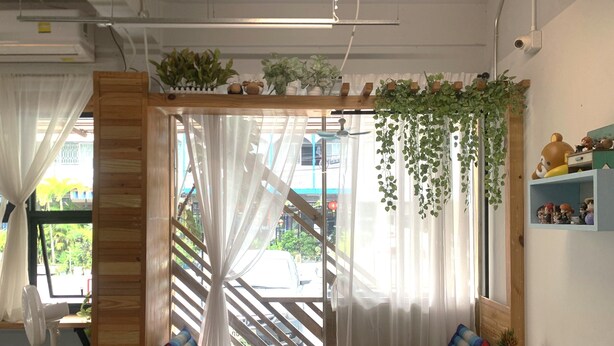 A cozy seating area with a wooden bench, cushions, and hanging plants. - Sleep Sheep Phuket Hostel SHA (Phuket)