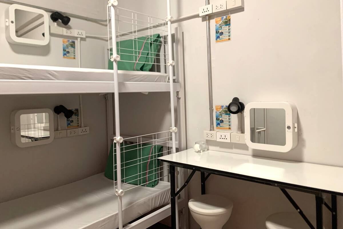 A bunk bed room with a small table, a mirror, and a toilet.