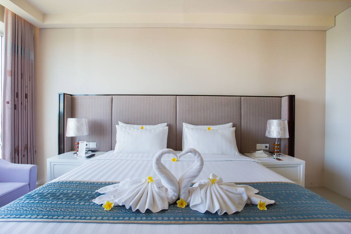 Habitación de hotel con una cama grande, dos mesitas de noche, una lámpara sobre cada una y un arreglo decorativo con forma de cisne sobre la cama.