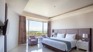 A modern hotel room with a large bed, a TV, a small table, and a view of the cityscape.