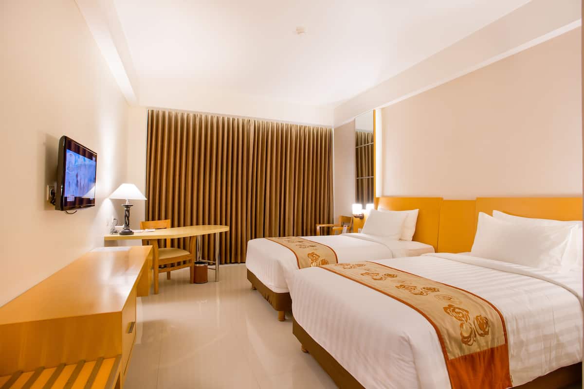 Habitación de hotel con dos camas, un escritorio, una silla, un televisor y una ventana con cortinas.