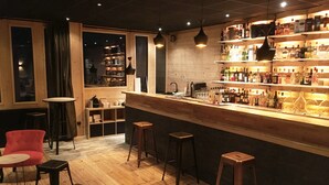 A bar area with wooden flooring, stools, and a bar counter stocked with bottles. - Hôtel La Mandia (Bagnères-de-Bigorre)