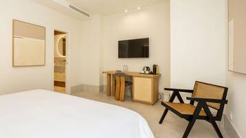 Habitación de hotel con cama, escritorio con silla, televisión y baño con espejo.