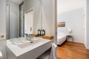 A modern bathroom with a large mirror, a sink, and toiletries. There is a wooden bench and a towel rack.