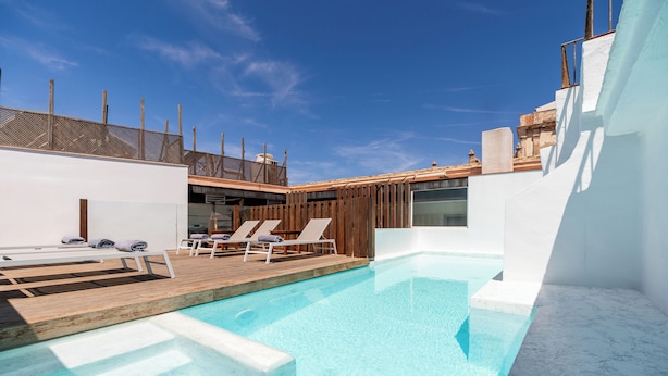 A modern outdoor swimming pool with wooden deck and lounge chairs, surrounded by white walls and a clear blue sky. - Hotel Aristoy-by Grupo Tribu (Tarifa)