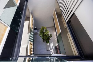 Un pasillo estrecho con barandilla de vidrio, una planta en maceta y vista a un edificio de diseño moderno.