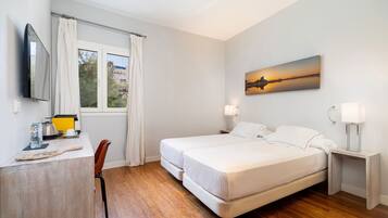 Habitación de hotel con cama, mesitas de noche, escritorio con silla, televisor y ventana con cortinas.