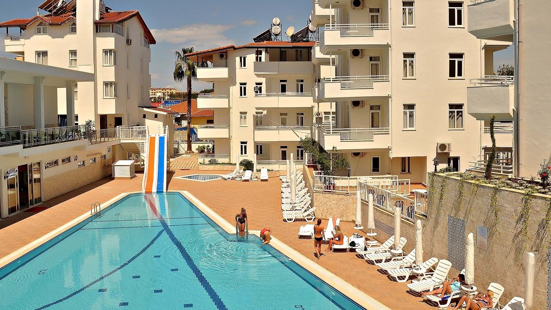 Una piscina con trampolino, circondata da sedie a sdraio e un edificio con balconi.