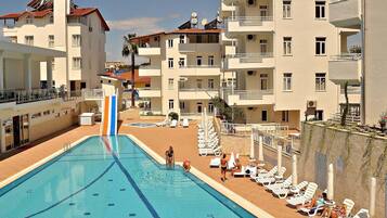 Una piscina con trampolino, circondata da sedie a sdraio e un edificio con balconi.