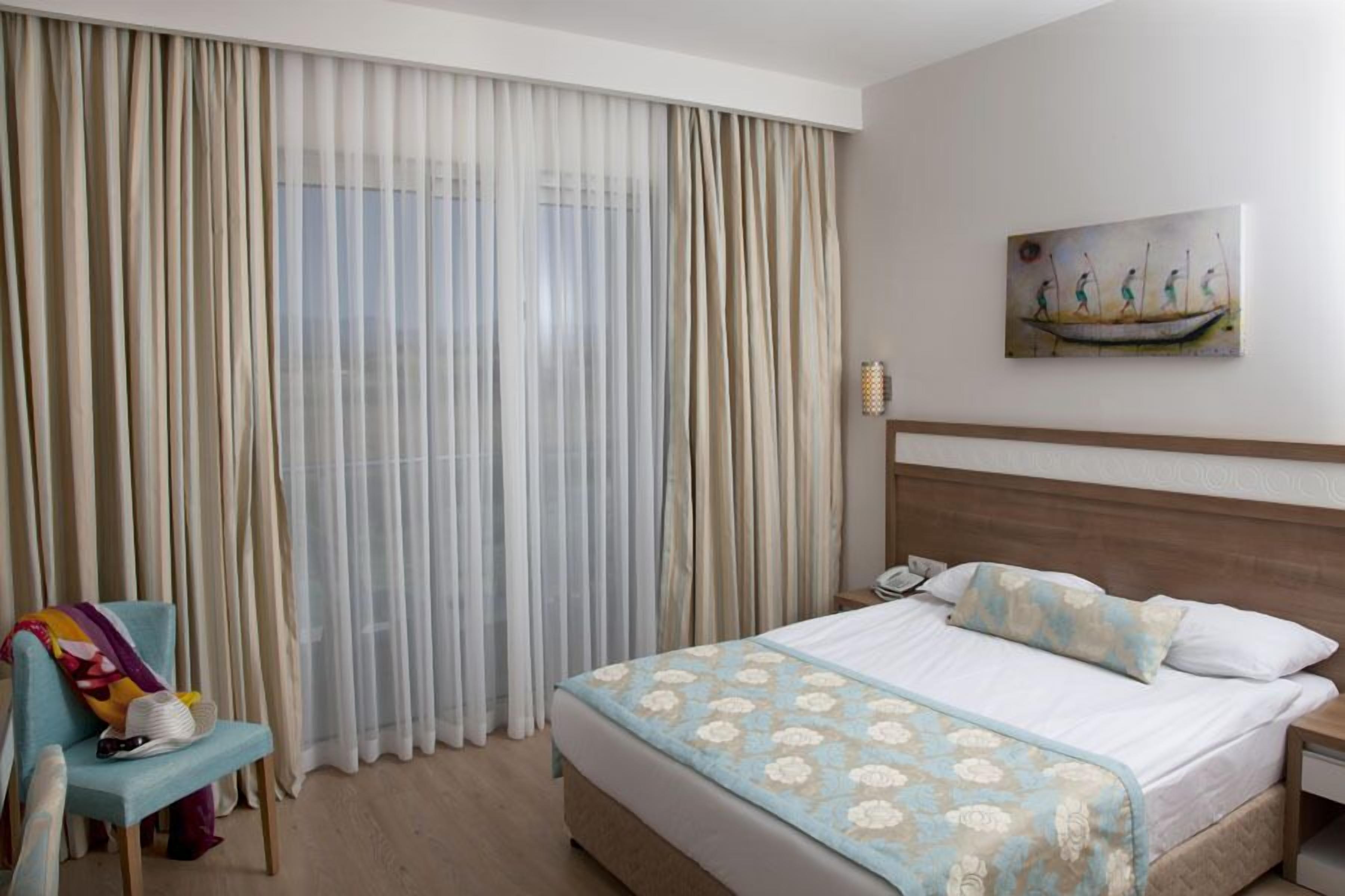 A hotel room with a large bed, a chair, a nightstand, and a painting on the wall.