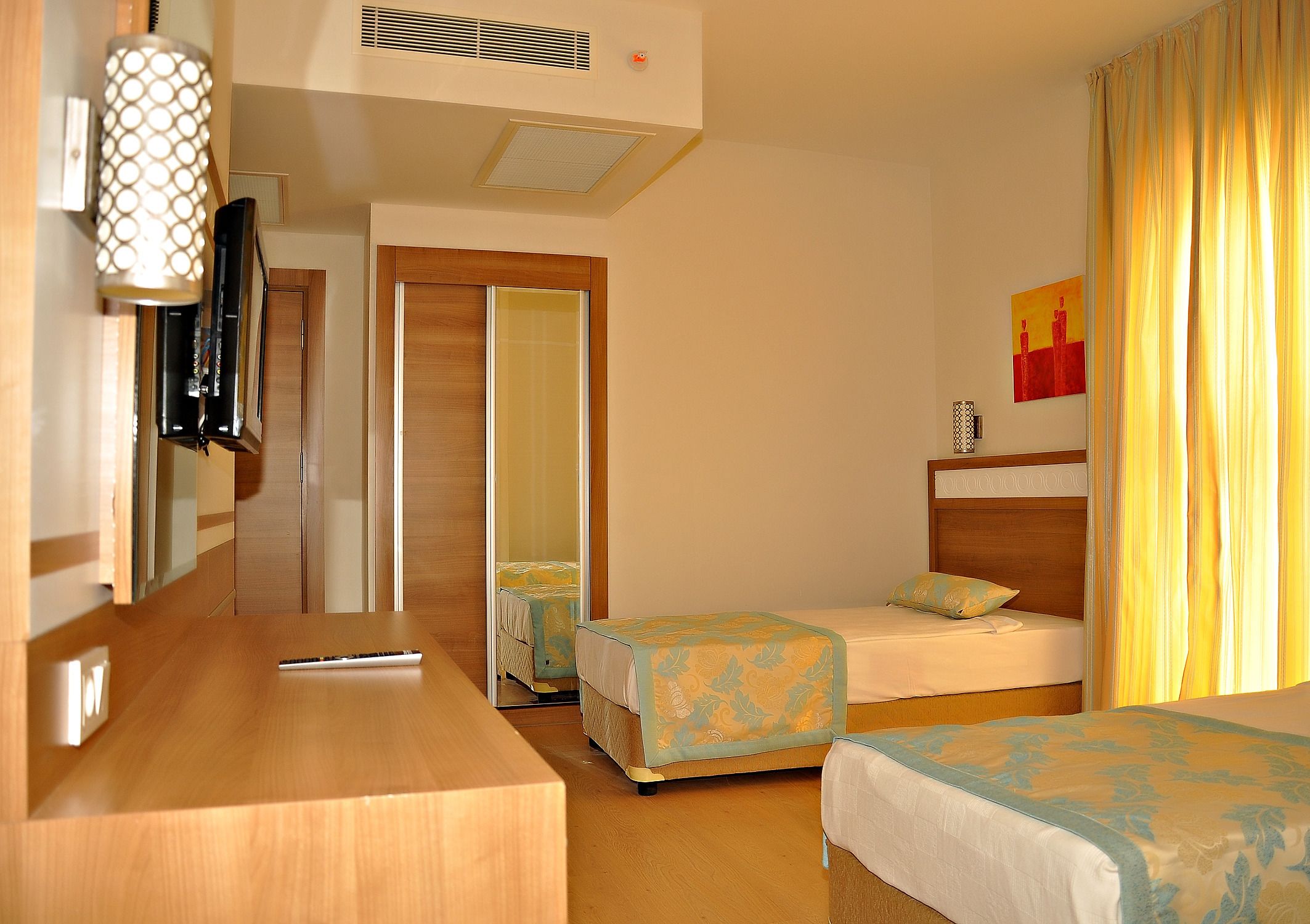 Ein Hotelzimmer mit zwei Betten, einem Holztisch, einem Spiegel und einem Bild an der Wand.