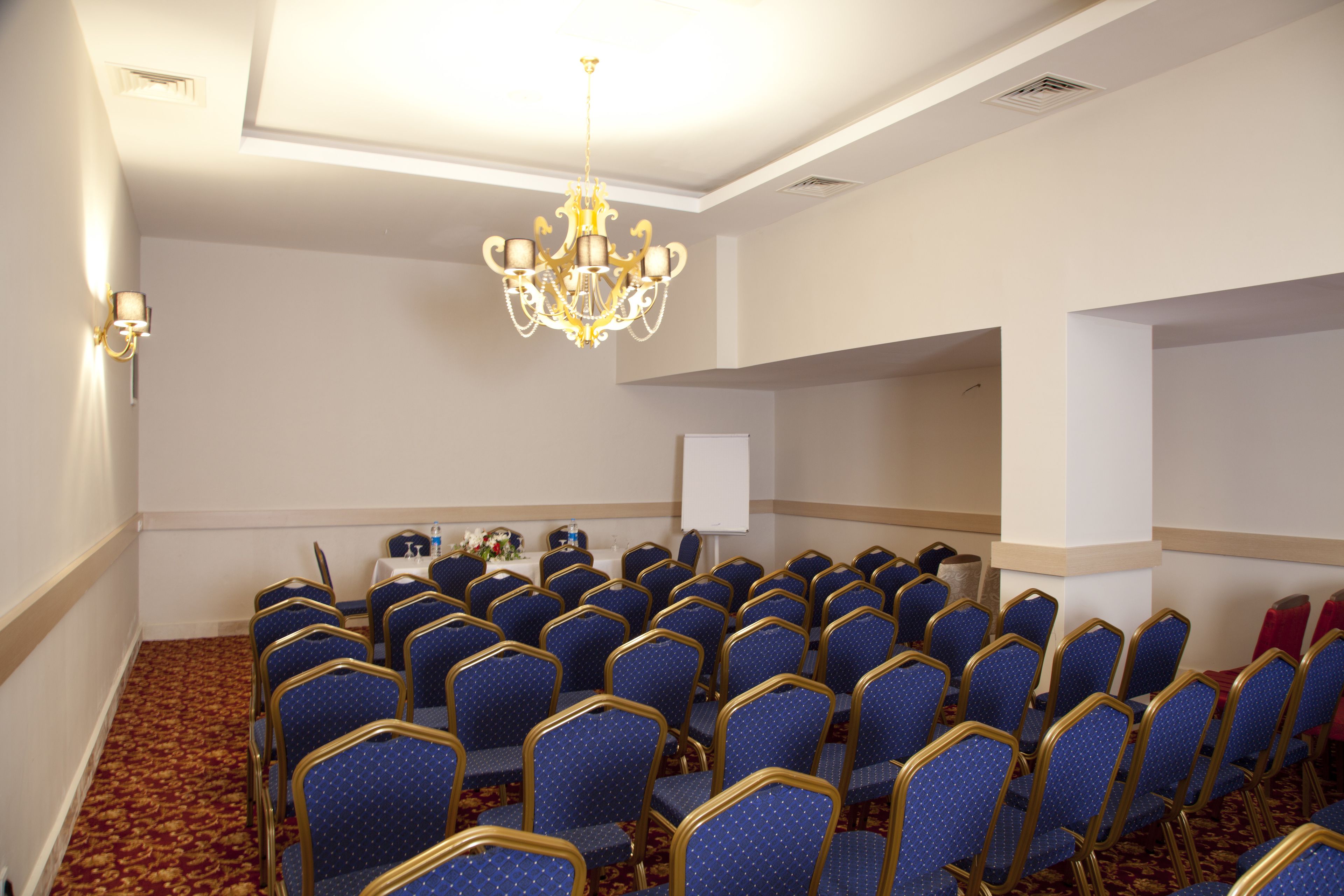 A conference room with rows of blue chairs, a chandelier, and a whiteboard.