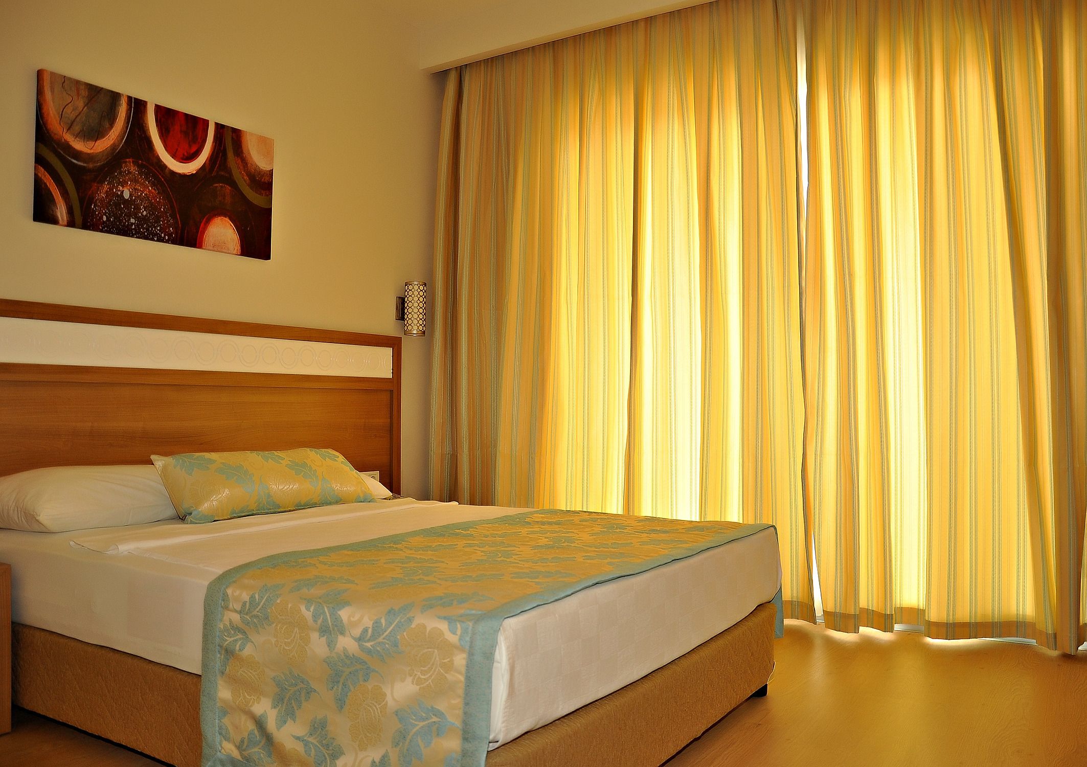 A hotel room with a bed, a headboard, a painting on the wall, and curtains.