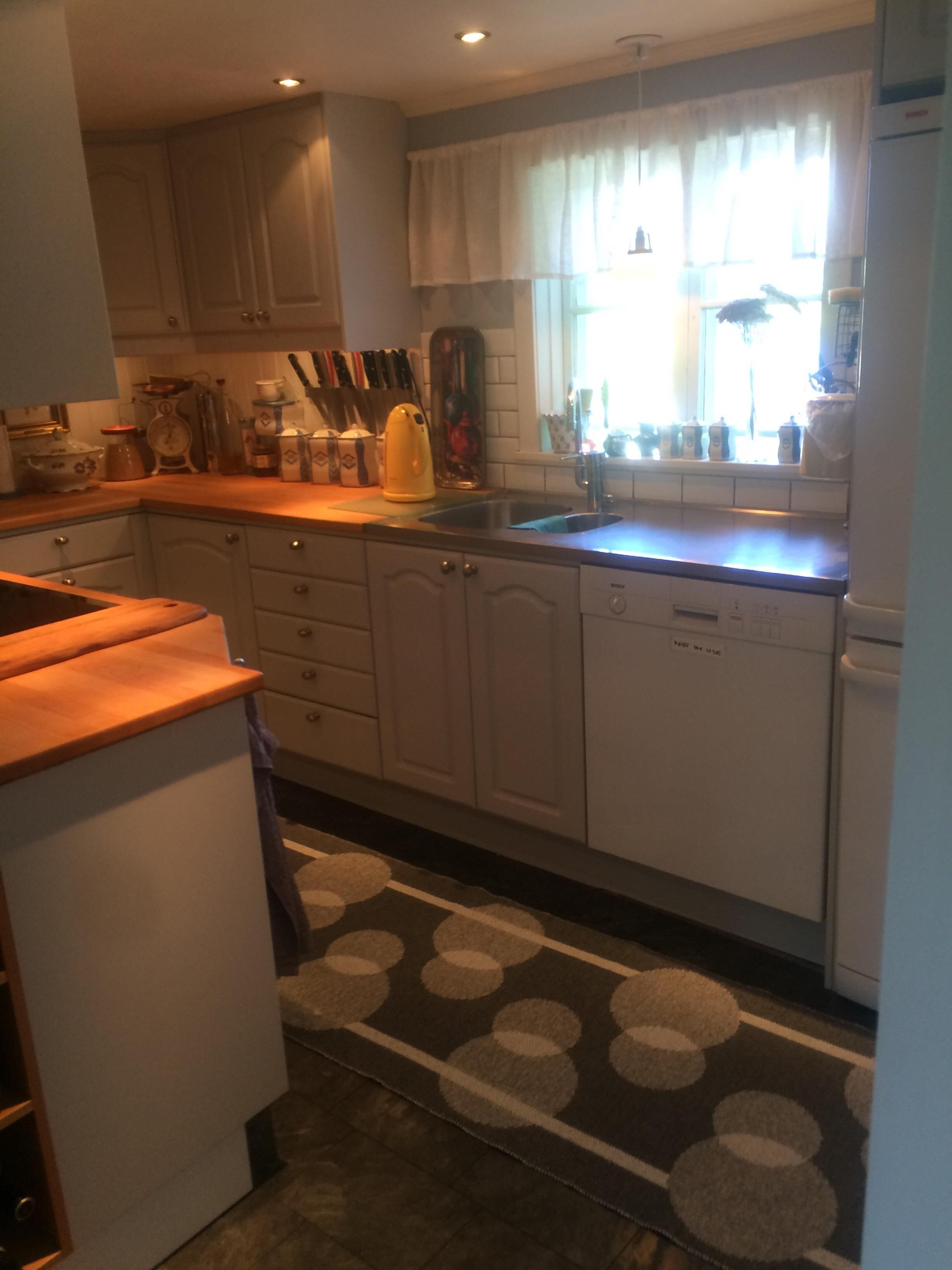 Una cocina con armarios blancos, un lavamanos y una ventana con cortinas.