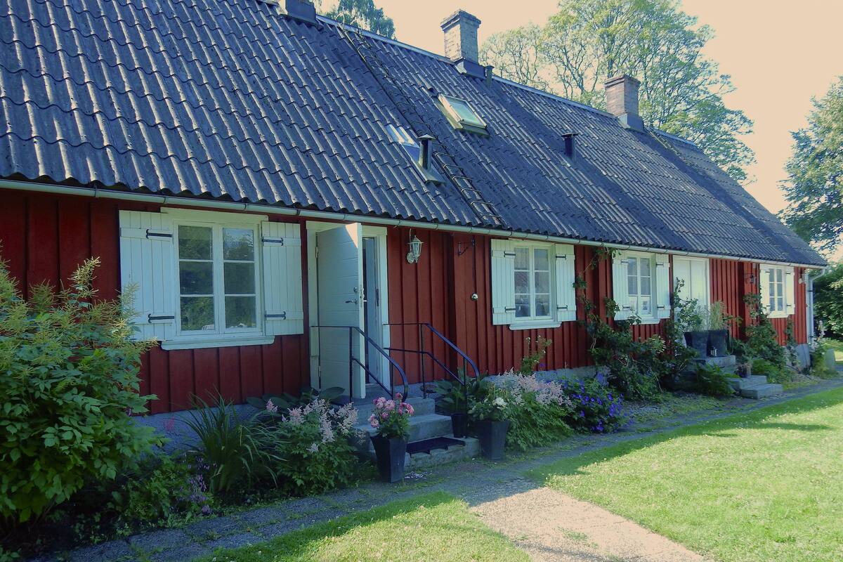 A red wooden house with a dark roof, white shutters, and a small porch with steps.