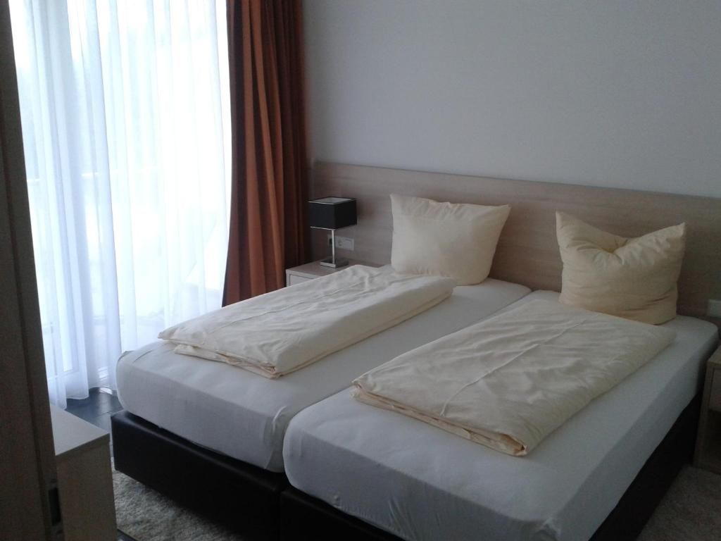 Een hotelkamer met een tweepersoonsbed, twee kussens, een nachtkastje met een lamp en een raam met gordijnen.