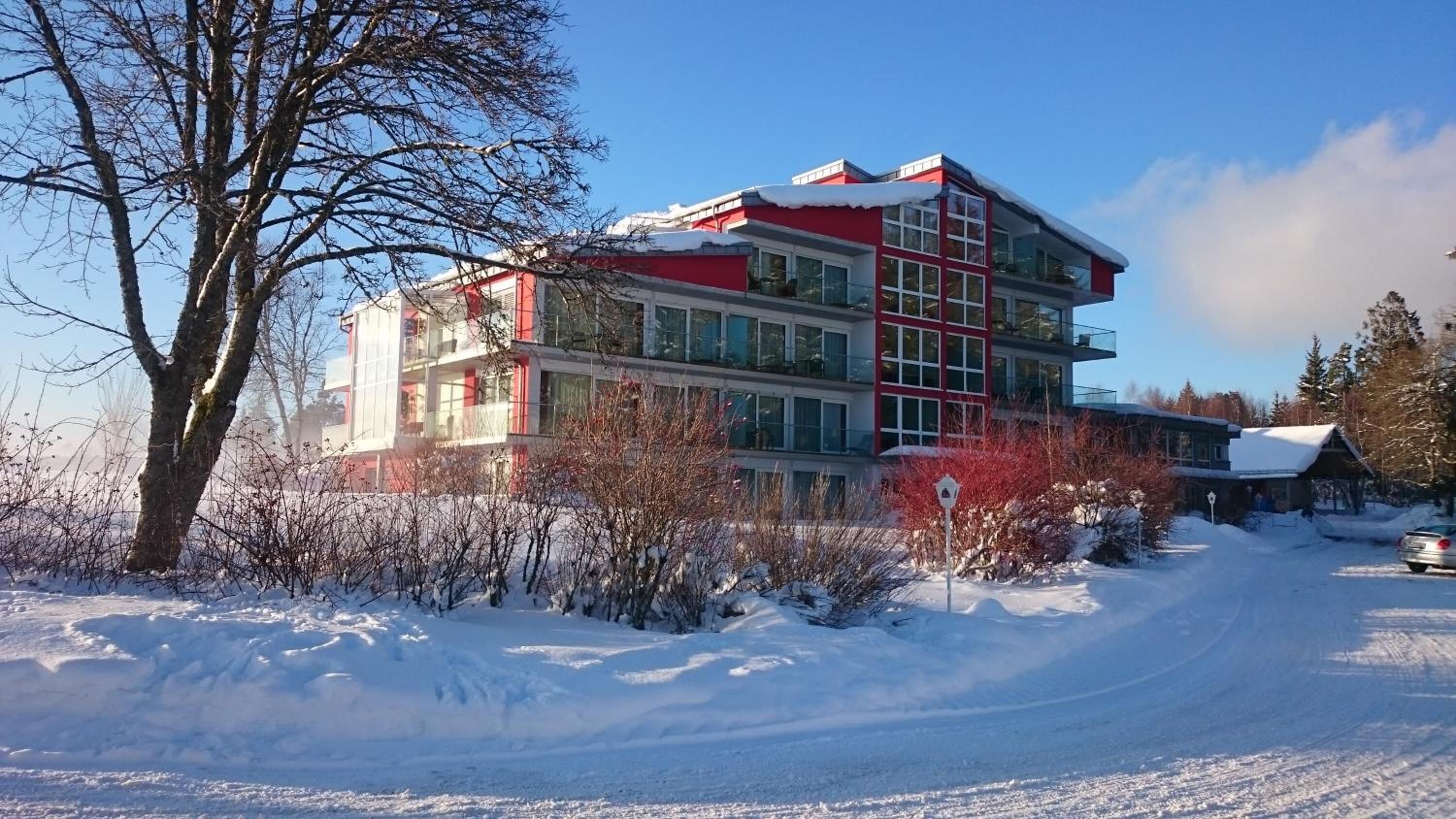 A multi-story building with a red and white facade, surrounded by snow-covered ground and trees.