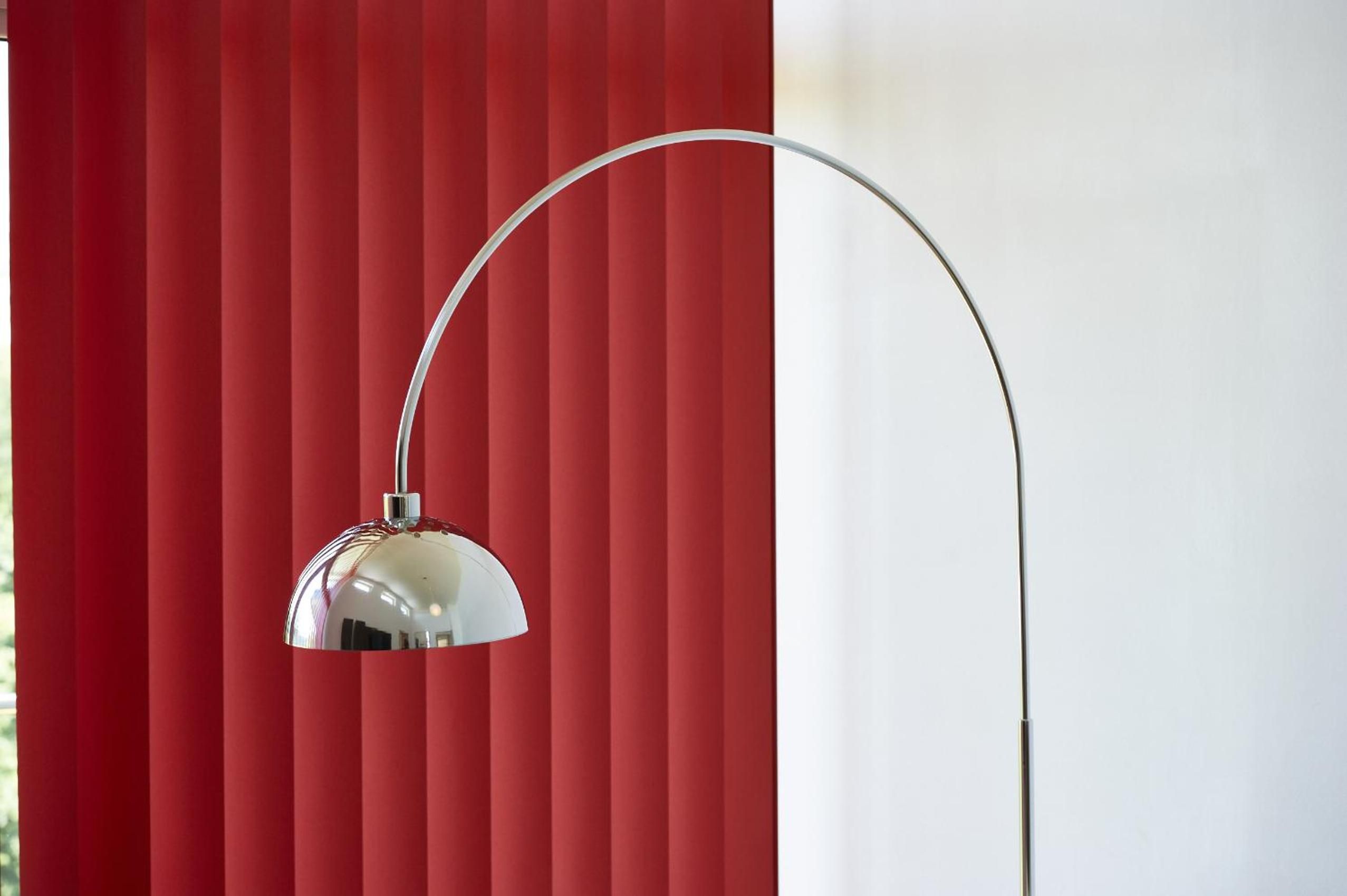 A floor lamp with a curved arm and a reflective shade against a red striped background.